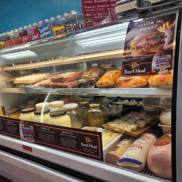 Deli display case filled with Boar's Head meats, prepared salads, and candy on the top shelf.
