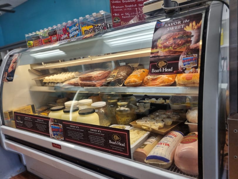Deli display case filled with Boar's Head meats, prepared salads, and candy on the top shelf.