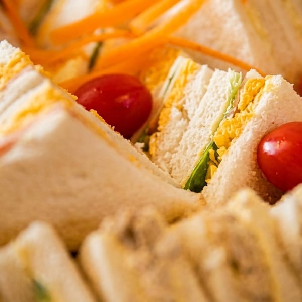 Close-up of triangular finger sandwiches with egg salad, lettuce, and cherry tomatoes.